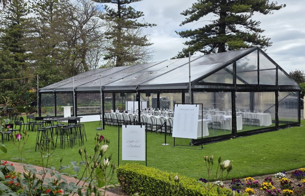 Party hire Adelaide -Elegant outdoor wedding setup in Adelaide with black frame and clear roof marquee, bentwood furniture, and custom signage