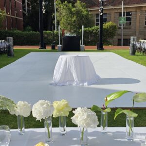 White dance floor installed on grass for an outdoor event with seating and ceremonial setup.