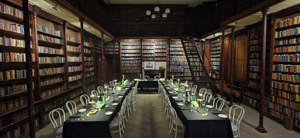 Sophisticated library dining setup with black tablecloths, white chairs, and candlelit centerpieces by Australian Hiring Company — premium indoor styling for Party Hire Adelaide events.