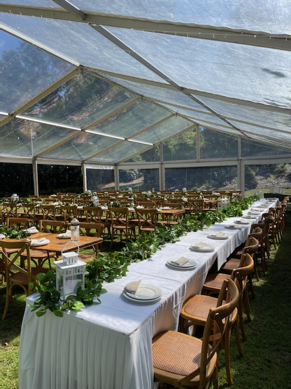Clear-roof wedding marquee with long timber chairs and white‑clothed tables styled with greenery, supplied and installed by Australian Hiring Company in Adelaide.
