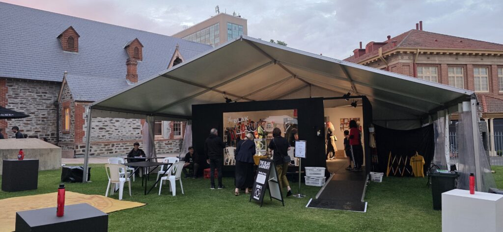 Outdoor event installation for Blak Laundry at AGSA featuring a white marquee, cultural display, clothing racks, guest seating, and event installation by Australian Hiring Company.